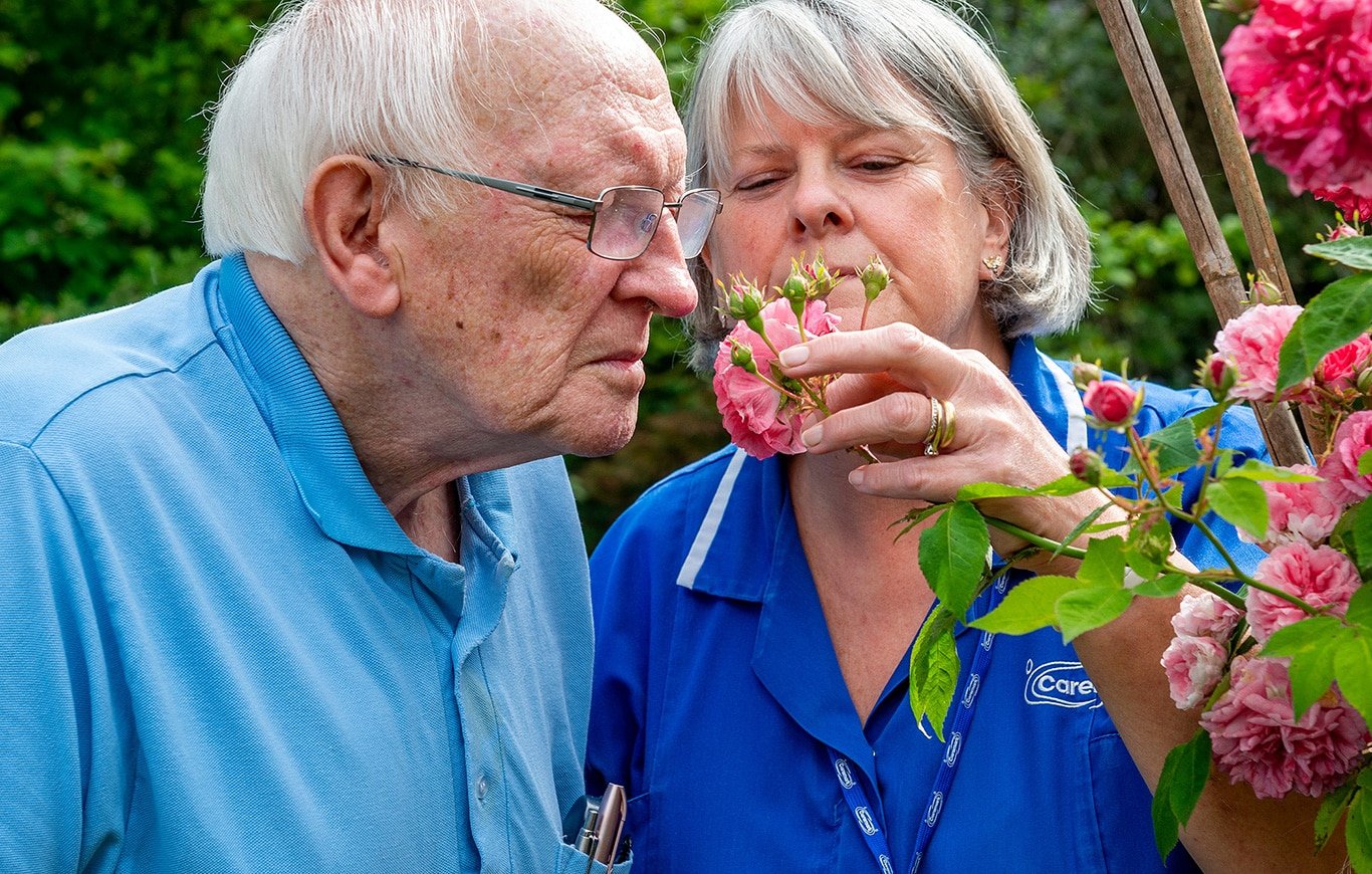 Elderly man and careworker smelling roses