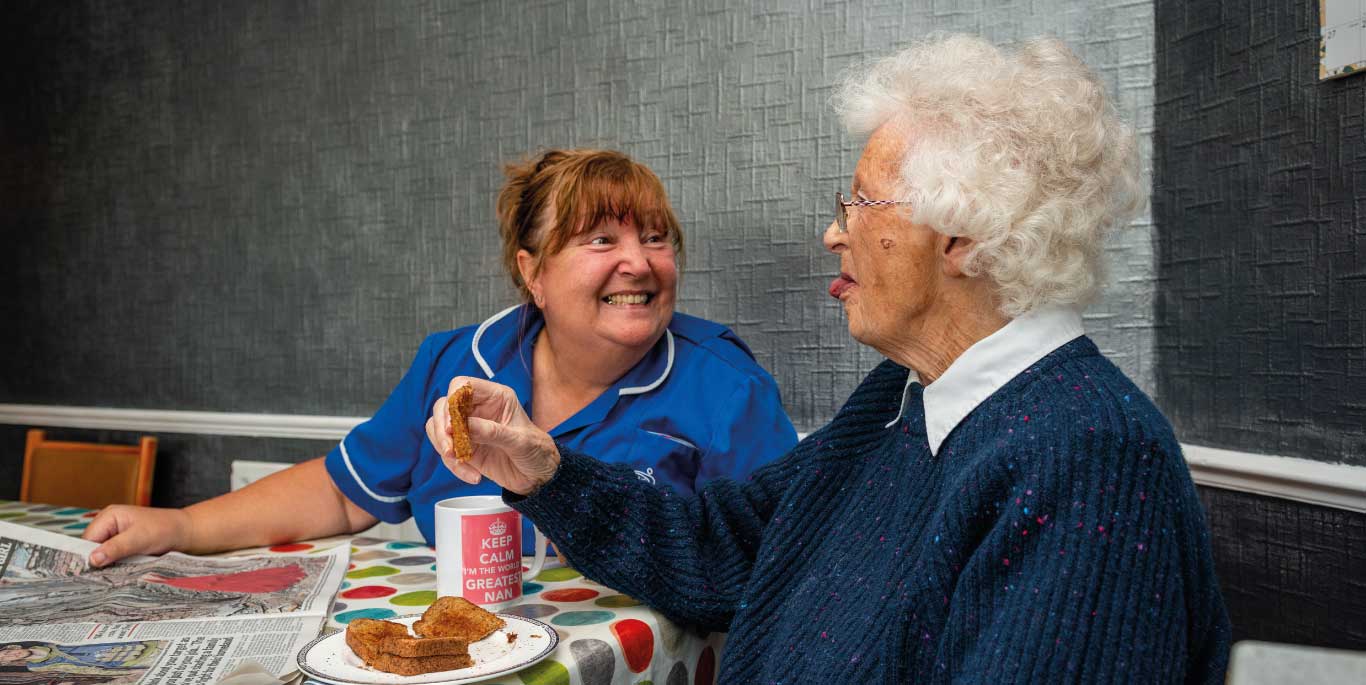 Dementia Care in Herefordshire : female care assistant and female customer eating toast