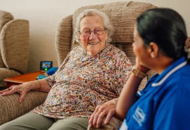 female care assistant is delivering complex care to female customer who is sat in her arm chair