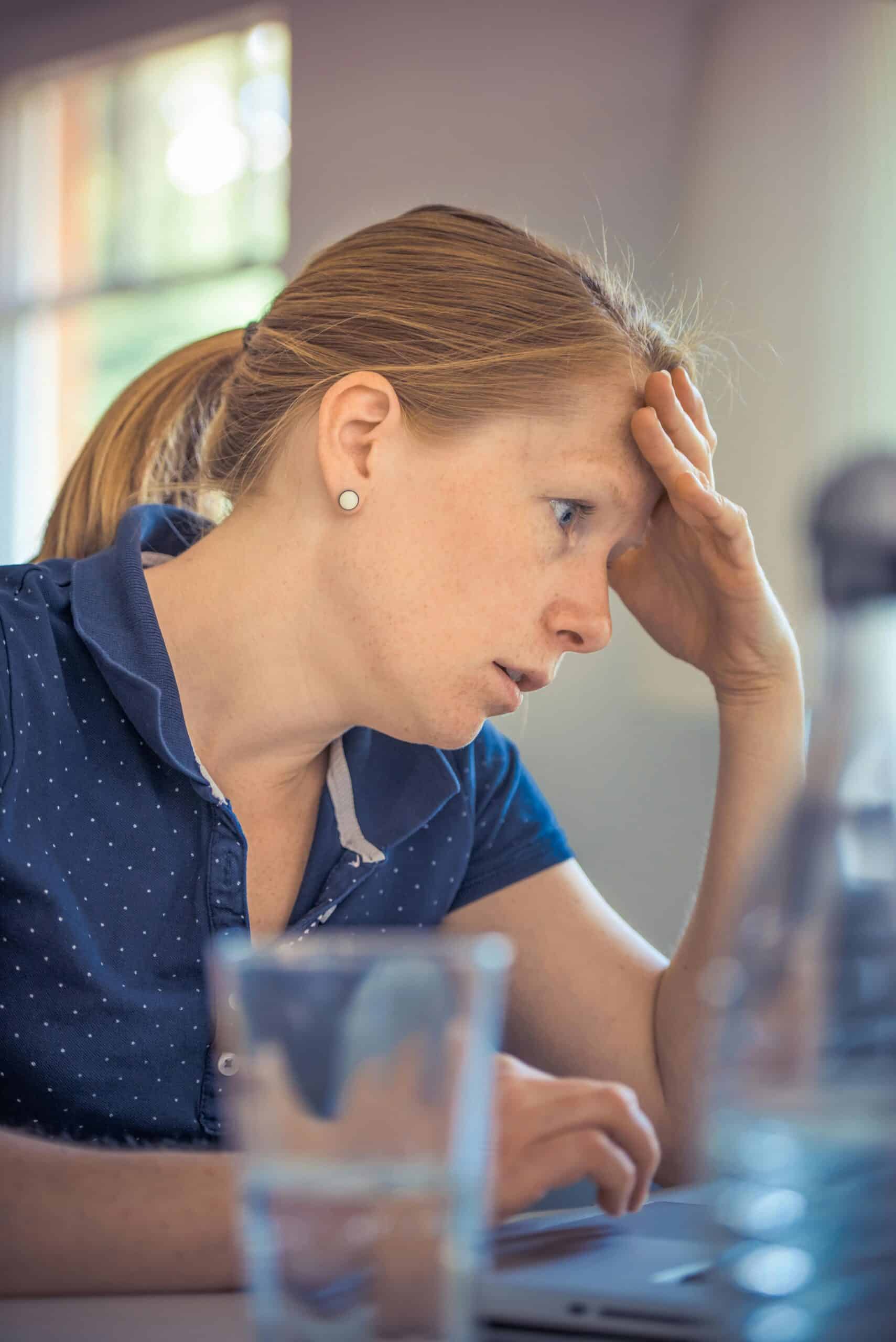 a woman wearing a blue shirt is holding her head with her hand, looking stressed