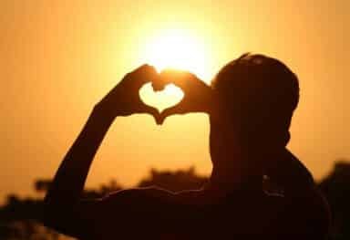 male making a love heart with his hands in the sunset