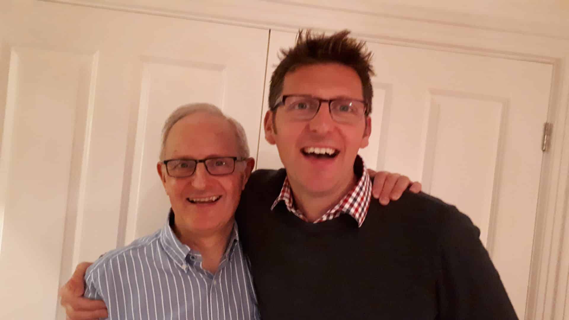 Two smiling men with arms around each other indoors, symbolising a family run Caremark franchise. Both are Franchise Owners and are father and Son.