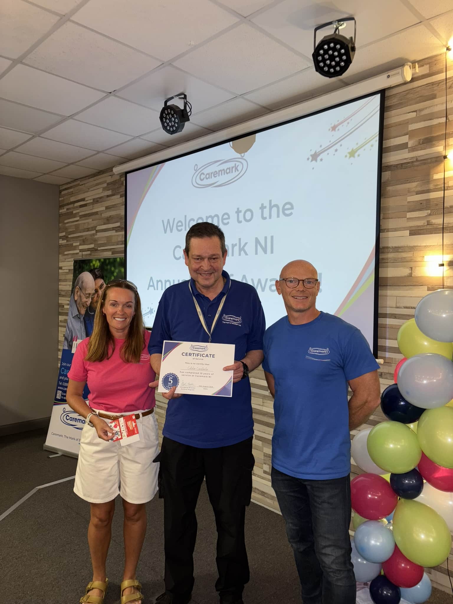 Employee smiling and holding his 10-year service certificate at Caremark NI