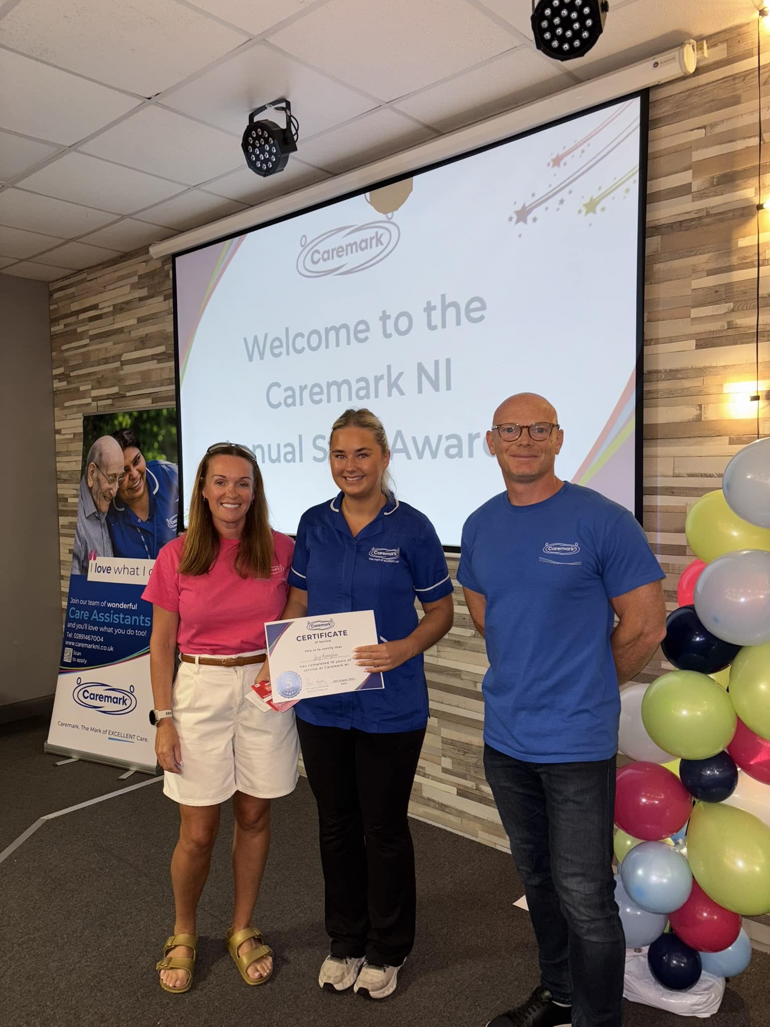 Employee smiling and holding her 10-year service certificate at Caremark NI