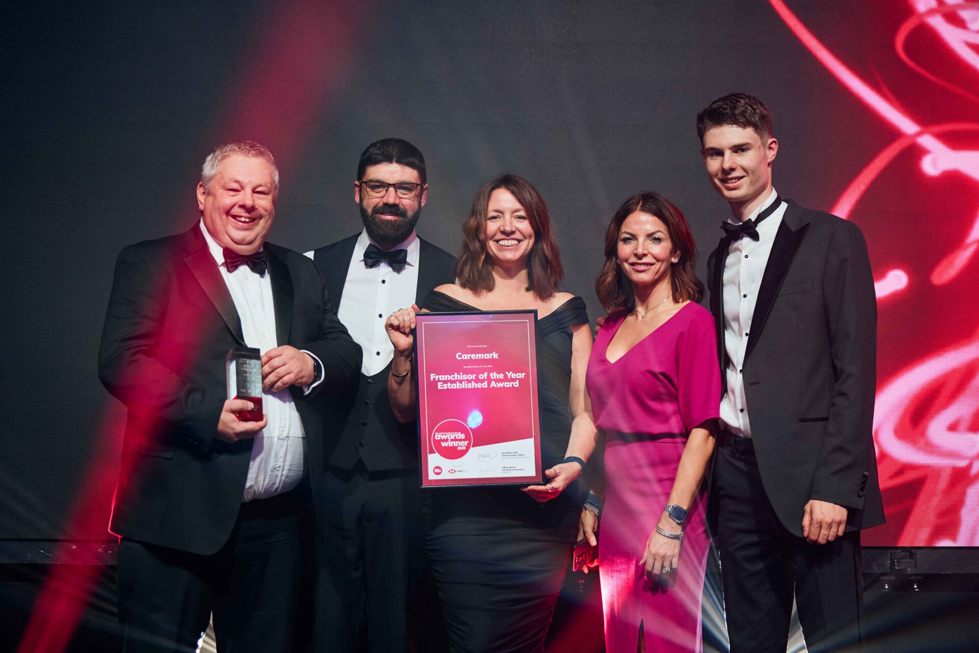 Caremark CEO & leadership team on stage accepting the BFA Franchisor of the Year Established award, holding the winner certificate under celebratory lights