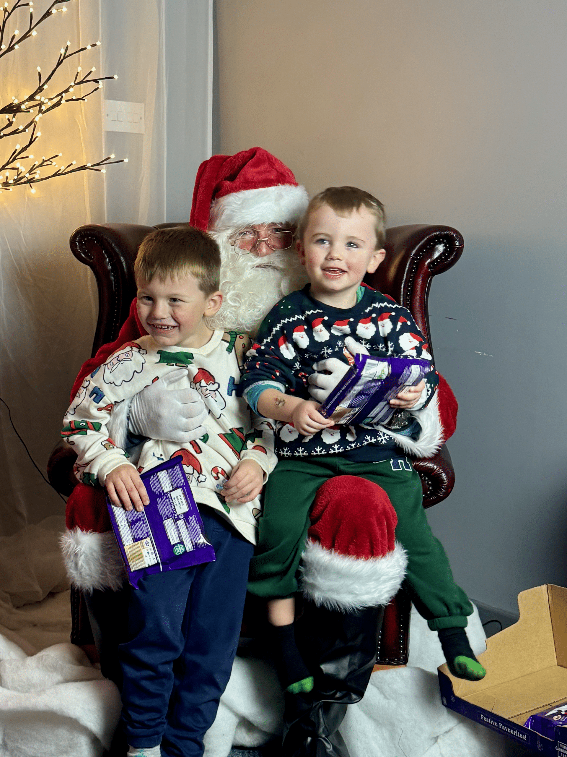 Two boys sitting on Santa's lap, smiling and enjoying a festive moment