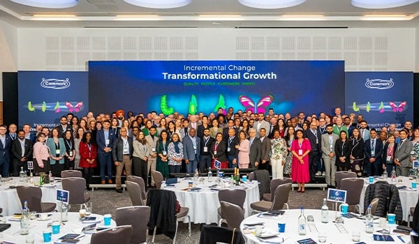 Caremark network group photo at a conference in a large event hall, with attendees standing in front of a stage screen reading “Incremental Change, Transformational Growth” and Caremark branding.