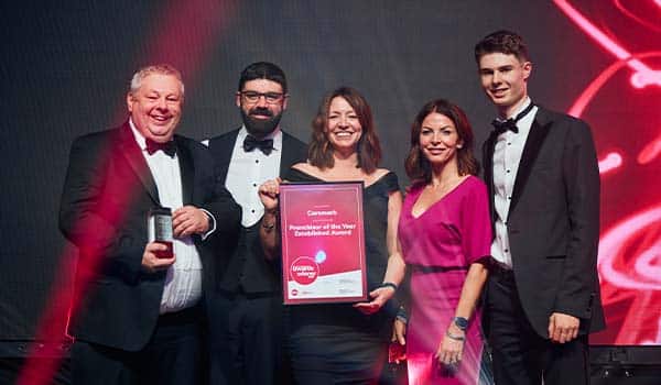 Caremark team on stage holding the BFA Franchisor of the Year Established Award certificate and trophy at an awards ceremony, dressed in formal evening wear.