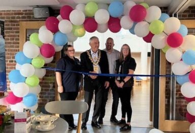 Caremark North Dorset and South Wiltshire office opening ribbon cutting under a balloon arch with Caremark team and a local mayor.
