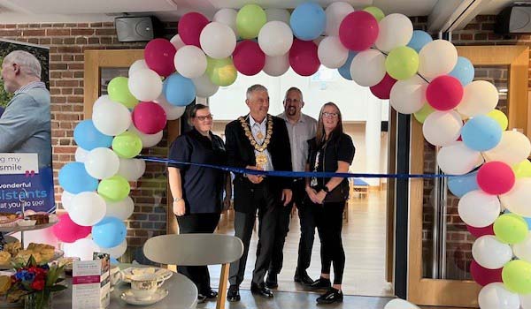 Caremark North Dorset and South Wiltshire office opening ribbon cutting under a balloon arch with Caremark team and a local mayor.