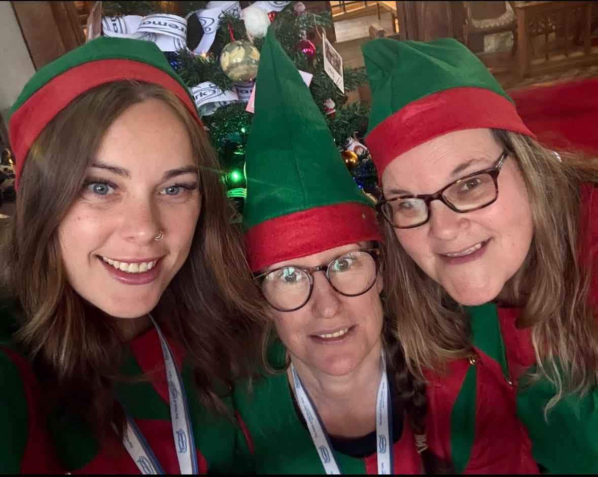 Caremark North Dorset and South Wiltshire team selfie in Christmas elf outfits in front of a decorated tree.