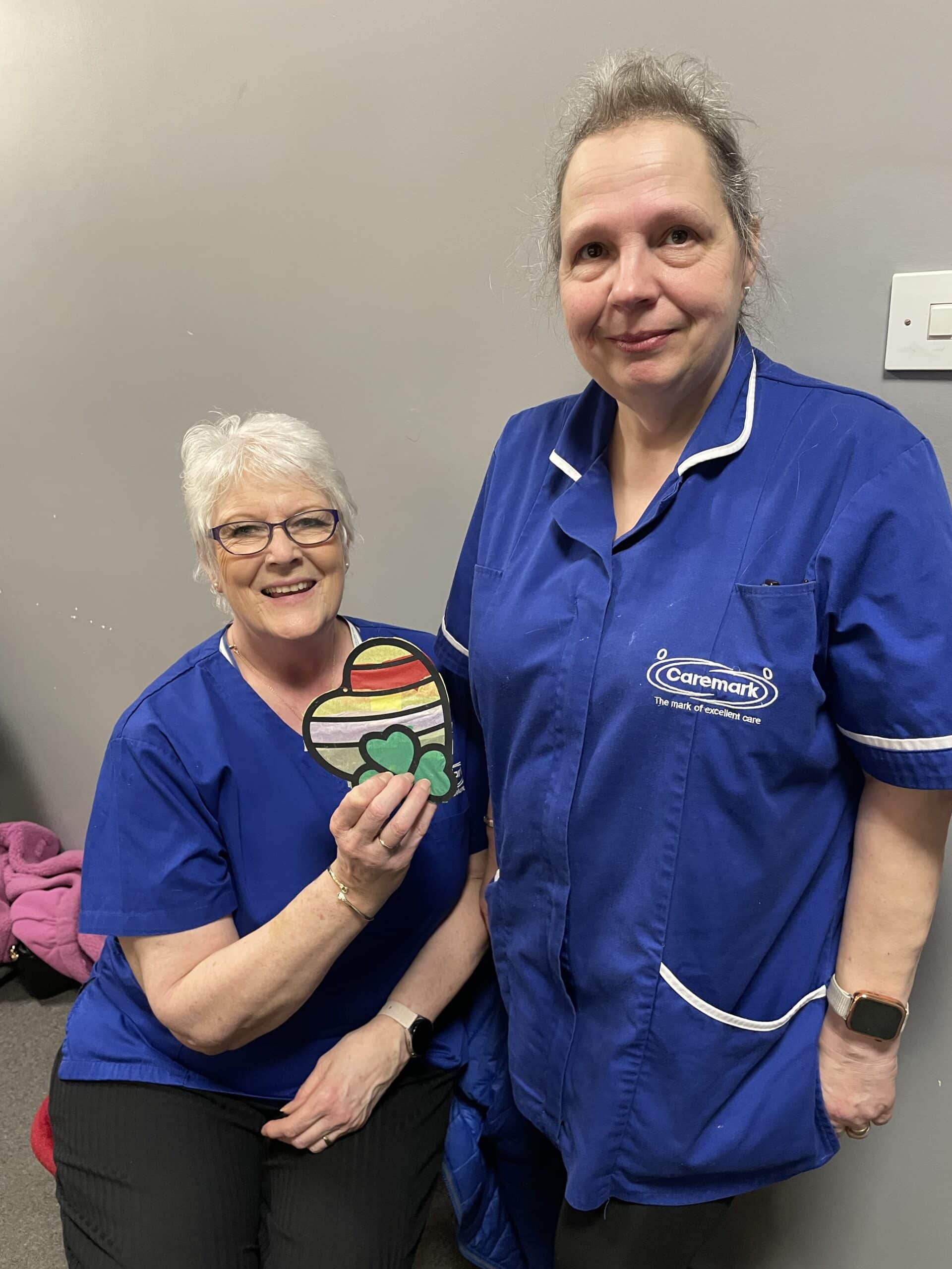 Two care assistants smiling and holding up a craft they made