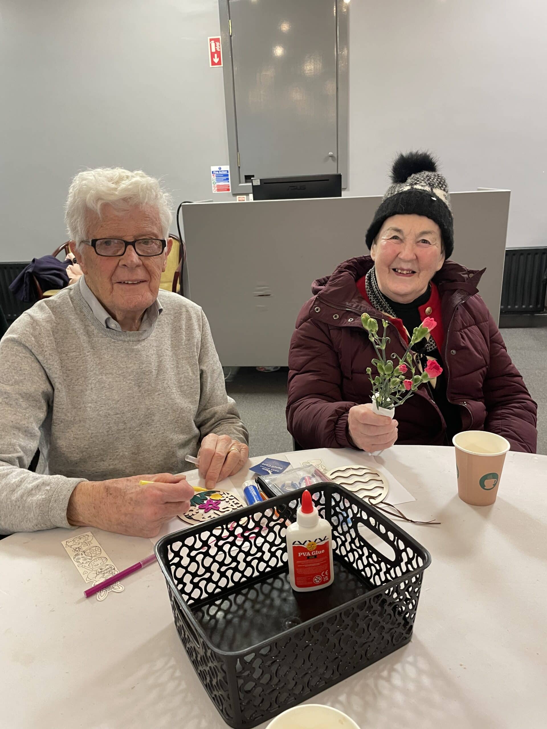 A woman and a man smiling while doing arts and crafts