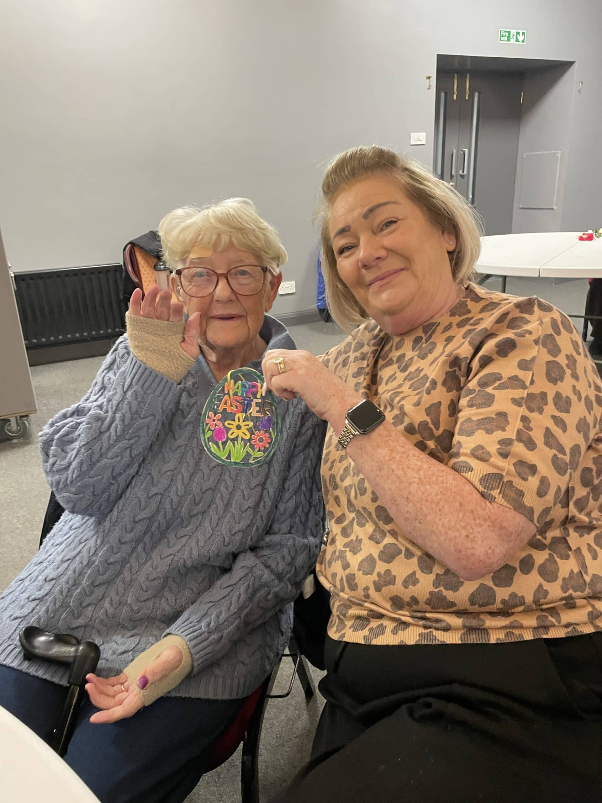 two women smiling and holding up a craft they made