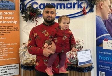 Kawan, franchise owner of Caremark North Norfolk and Great Yarmouth talks about being a young business owner in franchising and why he chose Caremark. Caremark office display with a young business owner holding a child, standing in front of Caremark signage and local home care materials.