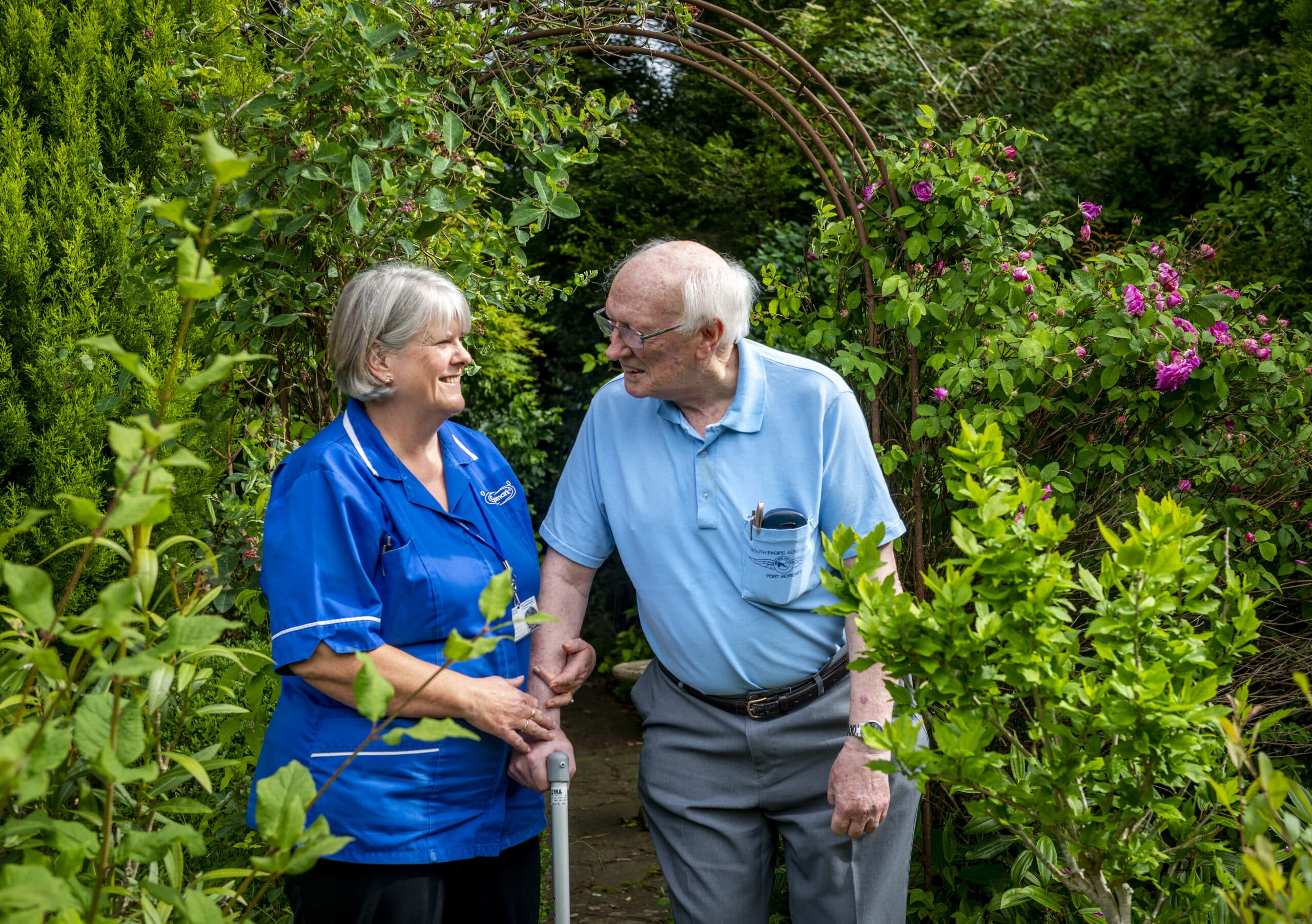Female care assistant and male service user smiling at each other in a garden