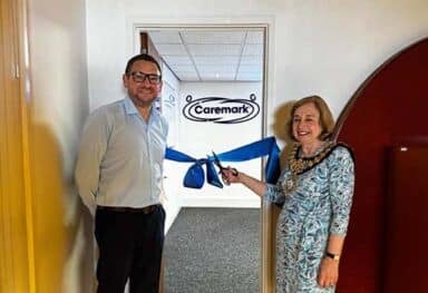 Domiciliary Care Agency Franchise office opening, with two people cutting a blue ribbon in front of a Caremark doorway sign