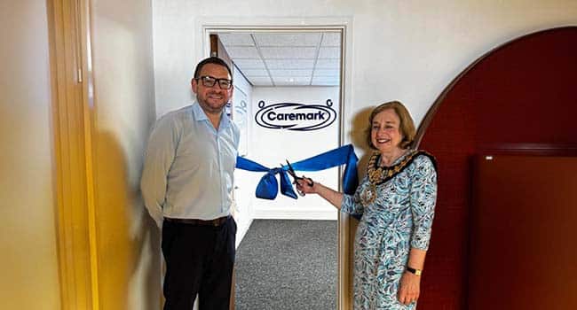Domiciliary Care Agency Franchise office opening, with two people cutting a blue ribbon in front of a Caremark doorway sign