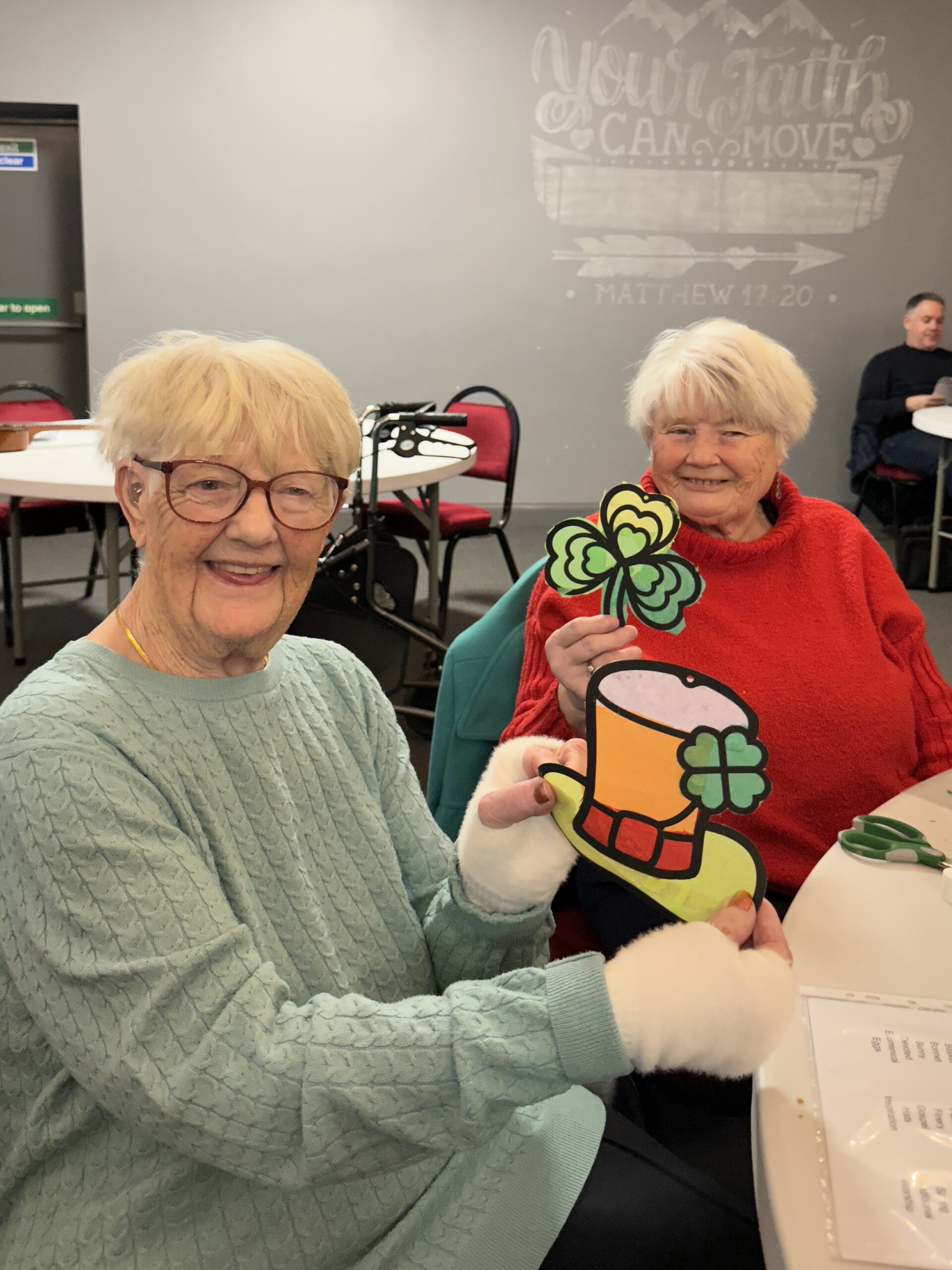 Service users smiling and showing off their St Patrick’s Day themed suncatcher made at the session