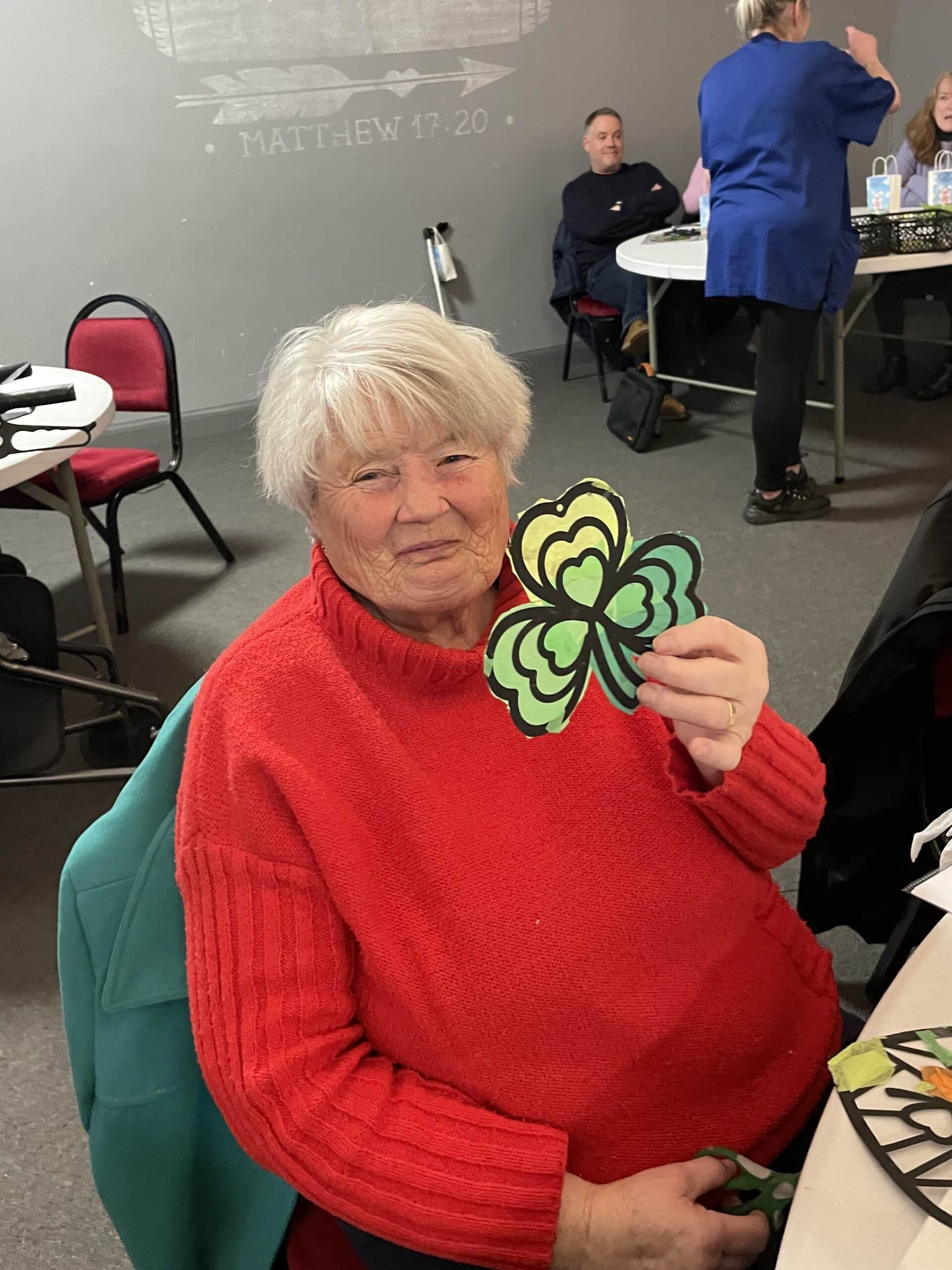 Service user smiling and showing off the St Patrick’s Day suncatcher she made