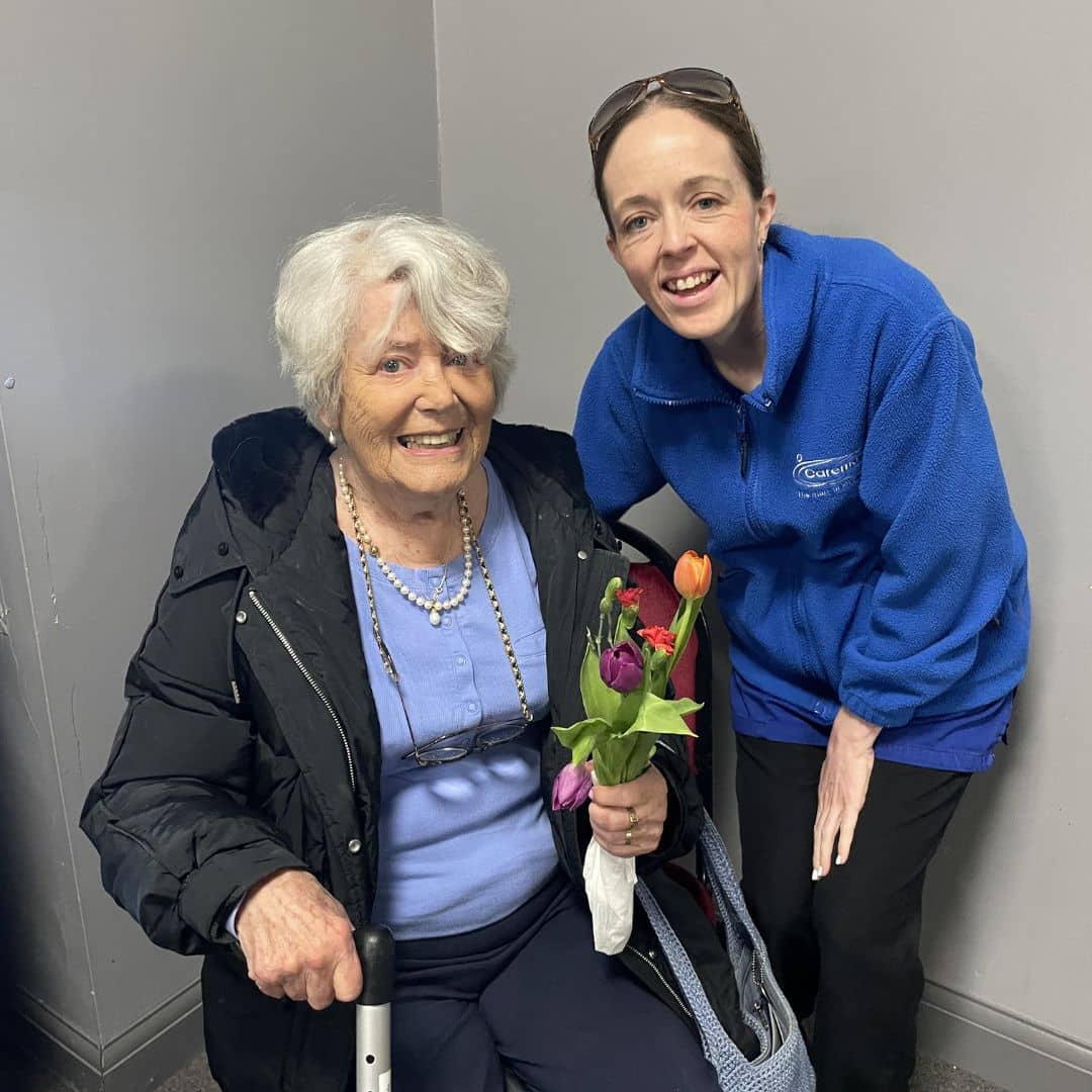 Service user smiling with flowers alongside a care assistant at the Memory Cafe