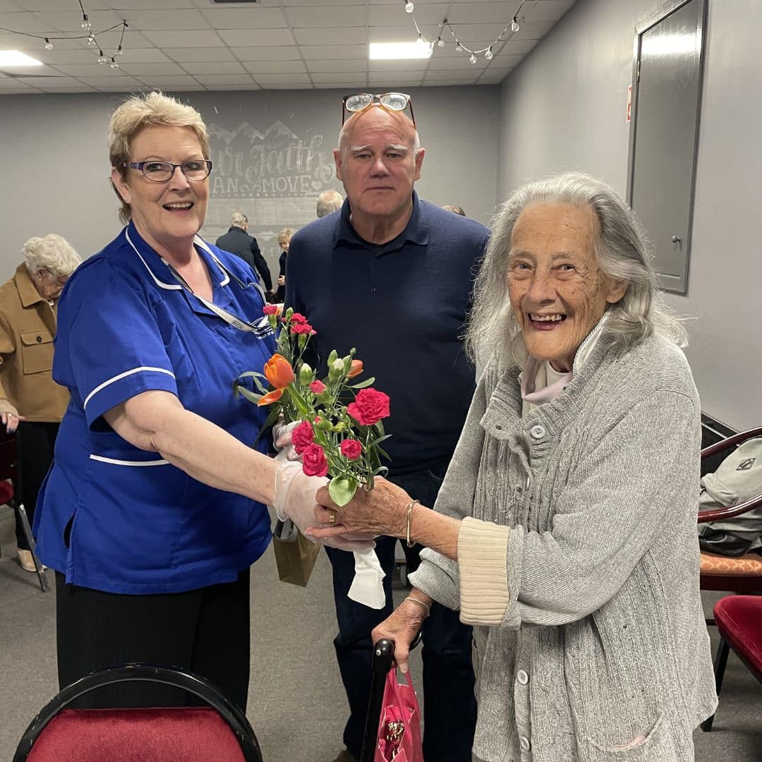 Service users smiling with flowers alongside a care assistant at the Memory Cafe