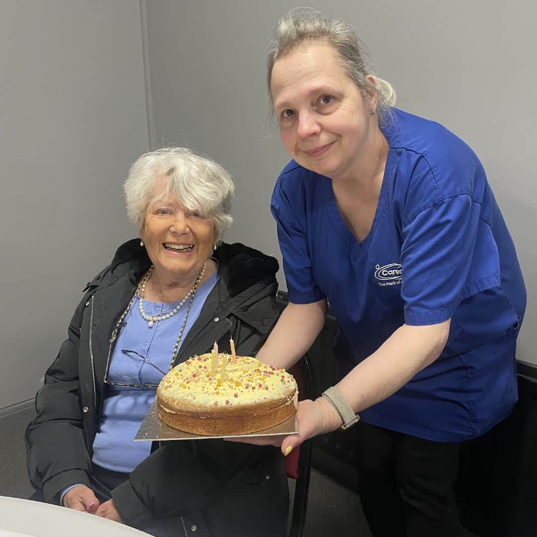 Care assistant and service user smiling with a birthday cake at the Memory Cafe