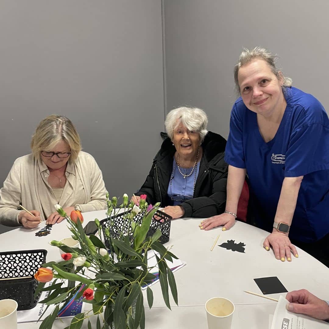Two service users enjoying arts and crafts with a care assistant at the Memory Cafe