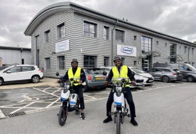 two care assistant on e-bikes wearing high visability jackets and helmets.