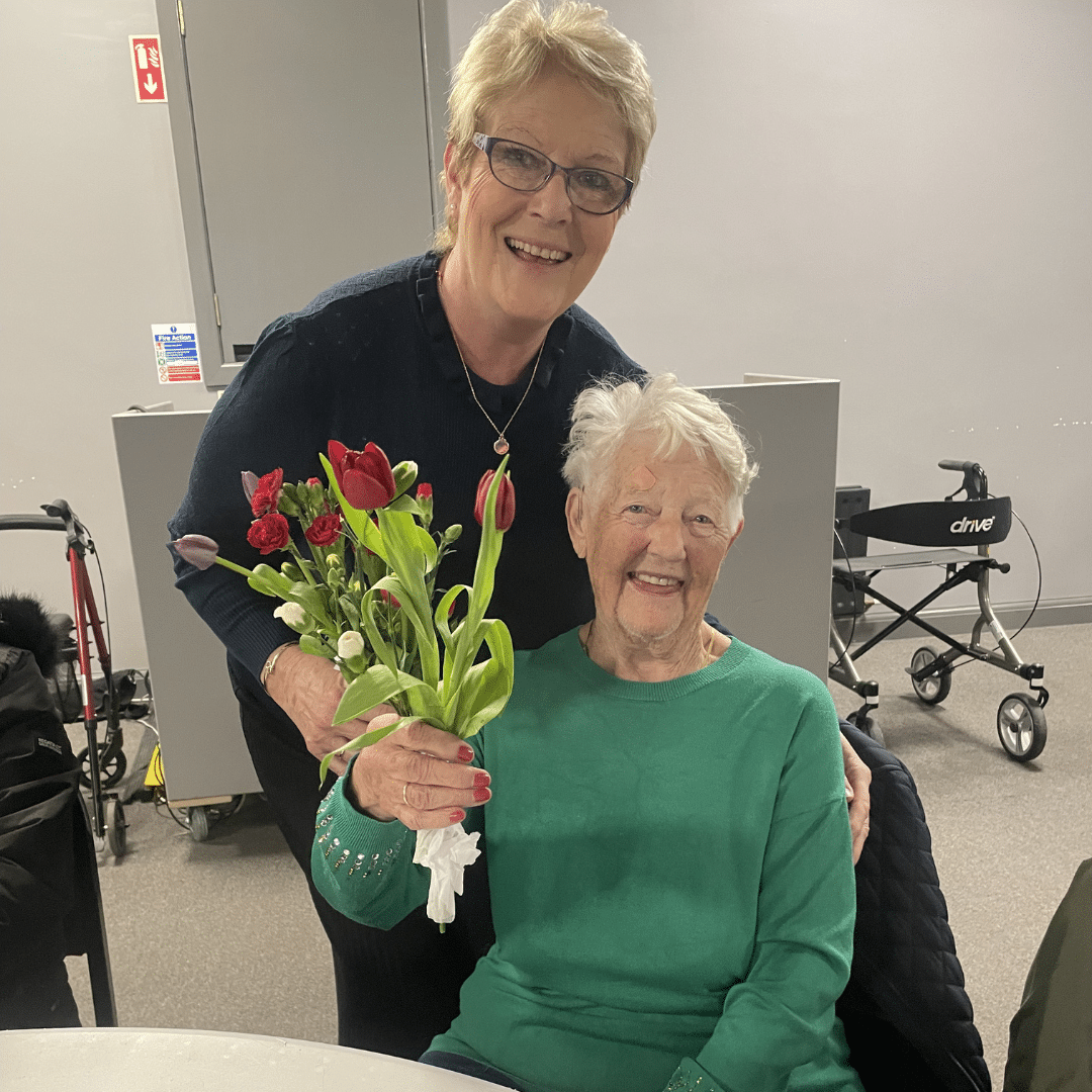 service user smiling with care assistant and holding a bunch of flowers