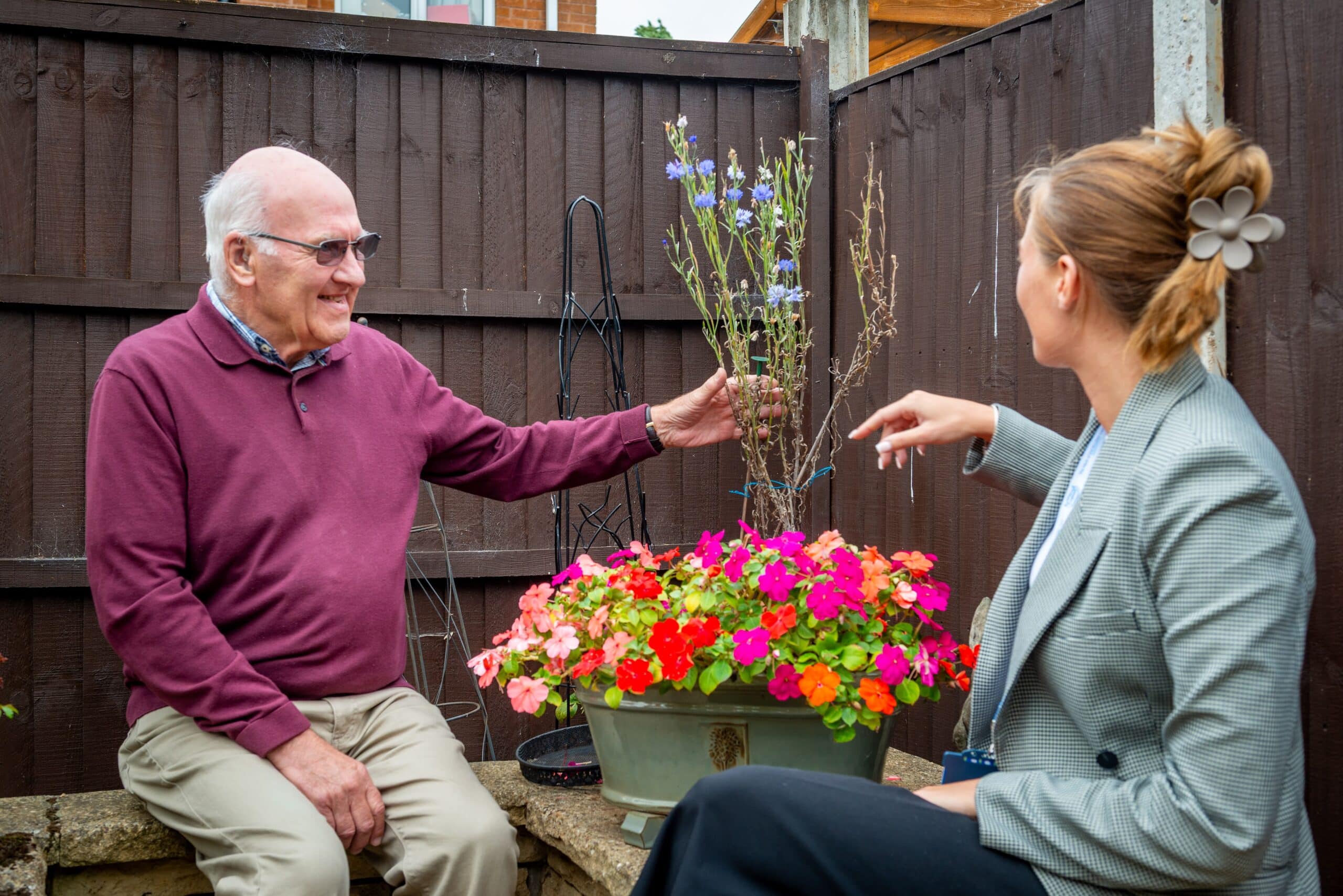 female care assistant supporting a smiling older male customer in taking care of the garden