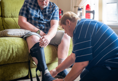 Female care assistant supporting male customer's injured leg after hospital stay