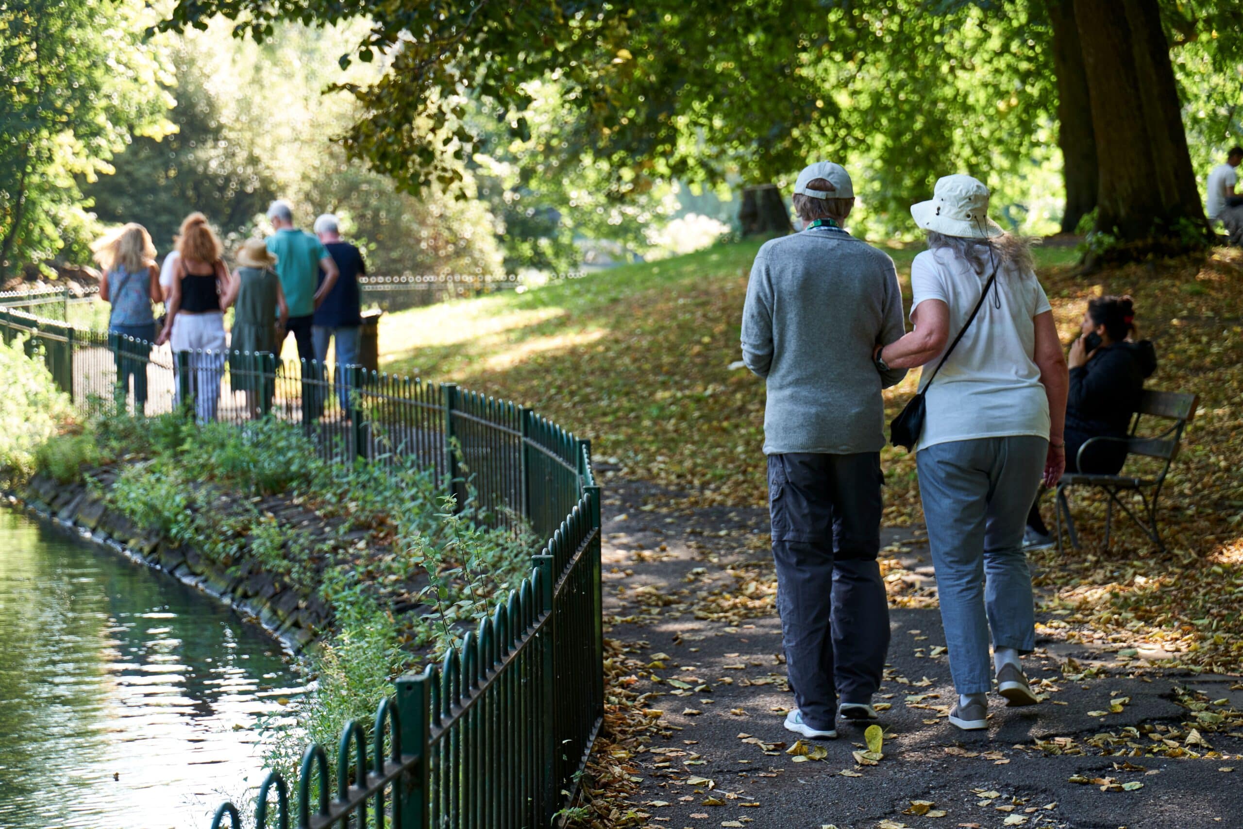 a younger gentleman supporting an older relative by walking hand in hand in a park surrounded by trees in York