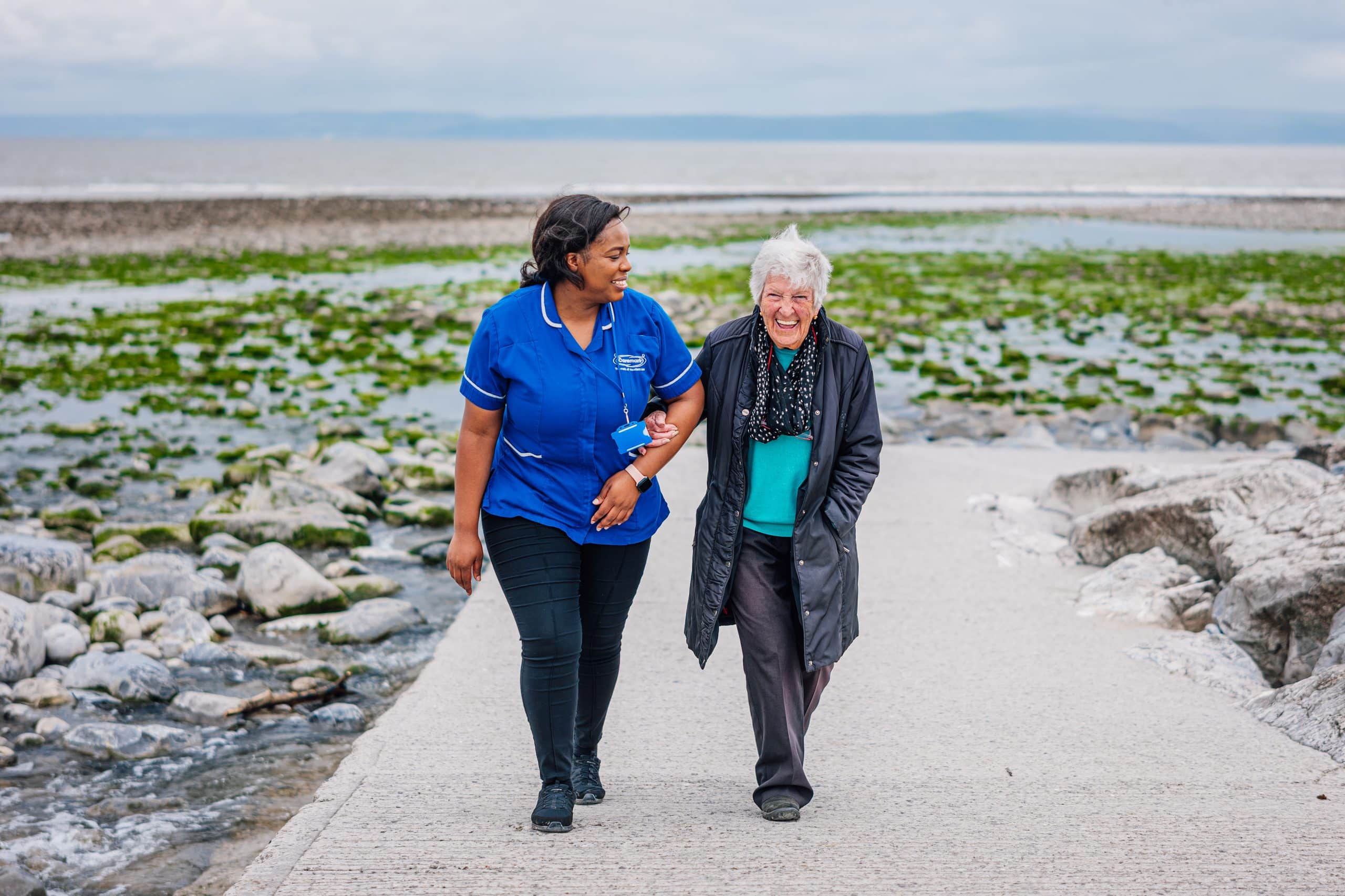 smiling older female customer enjoying a seaside walk with a Caremark care assistant, supporting mental wellbeing for older people in Scunthorpe.