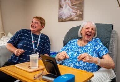 female customer laughing while sitting in her chair with a female care assistant laughing along side her