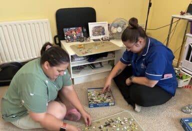 Family-like care in Cambridge as a Caremark Care Assistant and customer enjoy a jigsaw puzzle together at home.